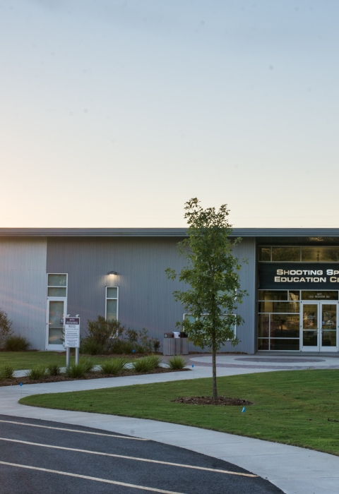 he left side of a brick-and-mortar buidling is illuminated by the sunrise peeping above the treeline.