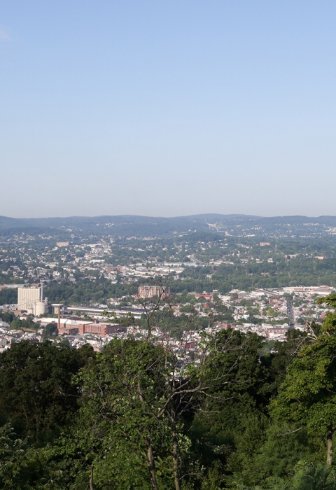 A landscape photo taken from a hilltop overlooks the town of Reading, Pennsylvania, below, with hills in the distance.