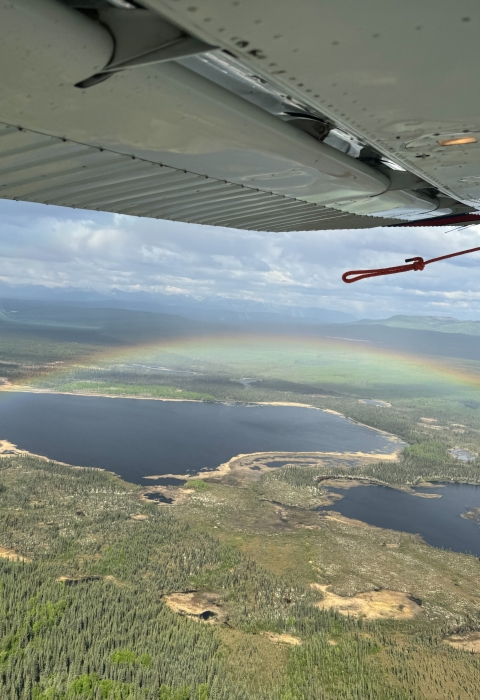 view of a rainbow over a landscape under an airplane wing