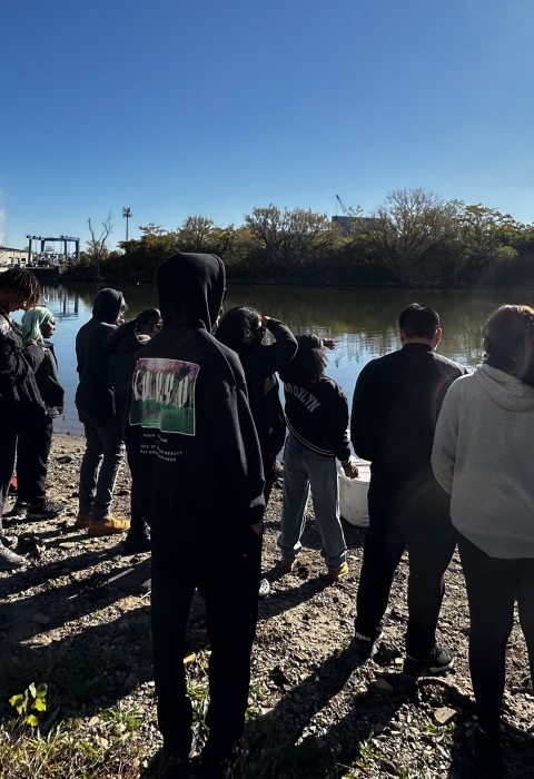 Image of students with teacher gathered along the shore with boat.