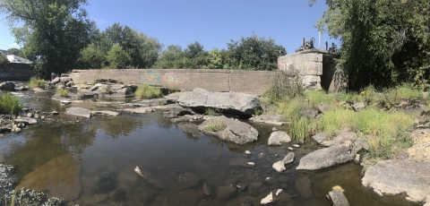 Concrete dam stands in a waterway. Left side of dam has been breached