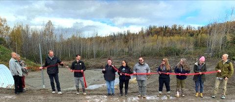 11 people cutting a red ribbon on a road with a stream in the background