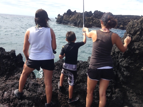 Women helps child cast fishing rod off rocky shore in Hawaii 