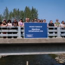 a group of people standing on a bridge over water holding a blue sign