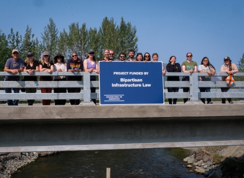 a group of people standing on a bridge over water holding a blue sign