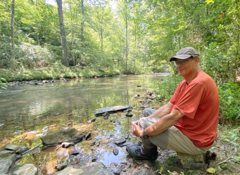 A man sitting alongside a creek.