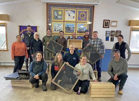 Fourteen people pose for a photo holding wooden boxes and frames with screens.