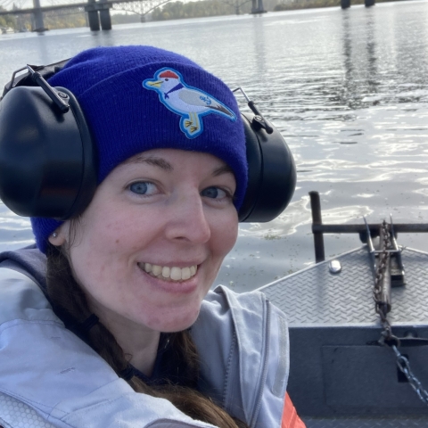 Selfie photo of woman on boat with blue beanie cap and hearing protection on head