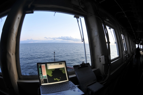 computer sits on a counter in front of a window looking out at the ocean