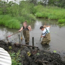 Two young people clear a beaver dam from in front of a culvert.