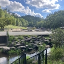 In the distance is a small building. In front of it is a series of concrete raceways, and a small stream.