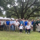 A large group of people pose for a photo outside in front of a large tree.