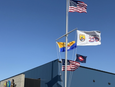 5 flags on flag pole with US at top; people stand beneath