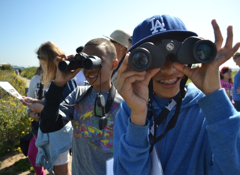 Smiling youngsters use binoculars to look at birds at San Diego Bay National Wildlife Refuge.