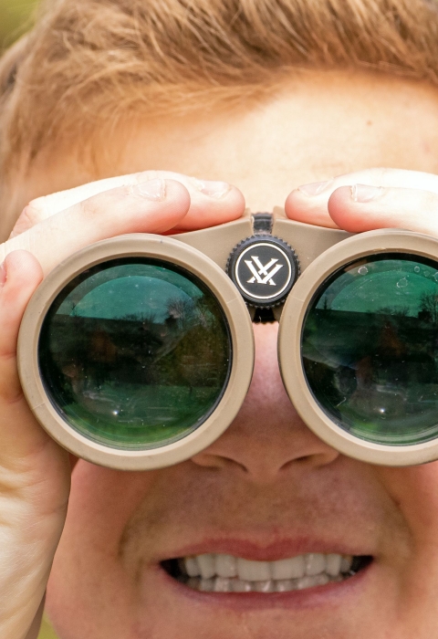 A red-haired boy looks at the camera through binoculars.