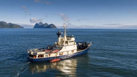 Blue and white ship sails on blue sea with green islands and blue sky.