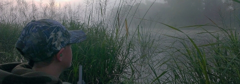 A younger hunter in camouflage looking out over a fog-shrouded marsh