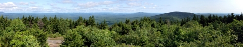 A scenic view of a hilly, forested landscape with light blue skies and a handful of small clouds