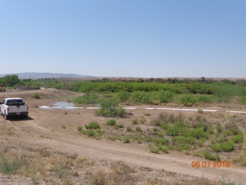 A white pickup truck near a pipe running through a field