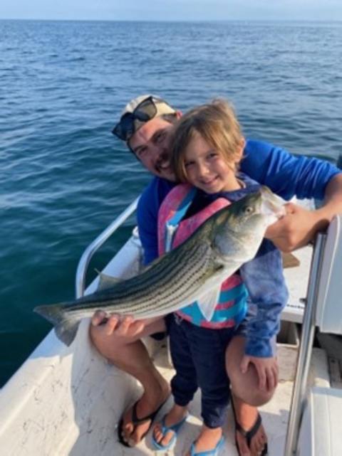 A man and child holding a fish while standing on a boat.