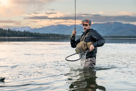 Man holds fly rod and net as he catches a trout.