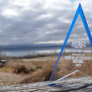 A translucent rectangular award sits in front of a lake and sagebrush habitat with an engraving that reads “Nampa School District New Partner Award Presented To Deer Flat National Wildlife Refuge 2023”