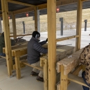 People sitting on wooden benches holding firearms and shooting at a range