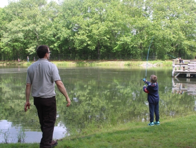 Service employee in refuge browns watches as young boy casts fishing pole into pond.