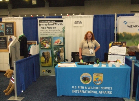 A woman stands behind a table with a tablecloth that reads U.S. Fish and Wildlife Service International Affairs