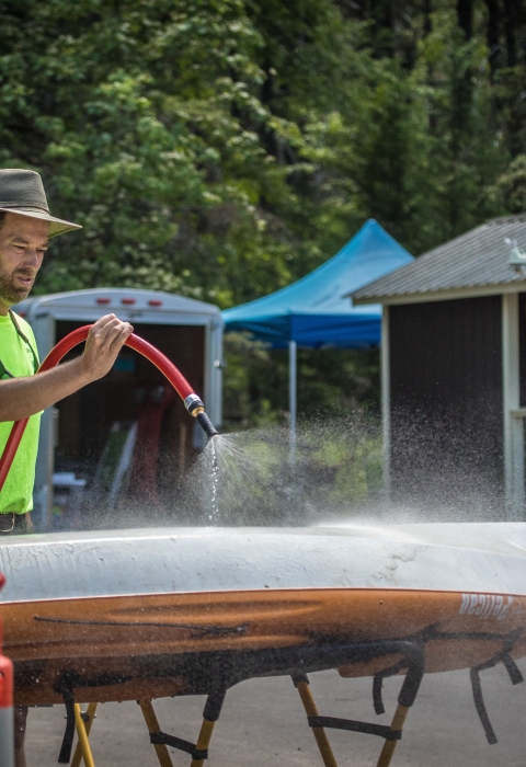 A man uses a hose to wash off the bottom of a kayak