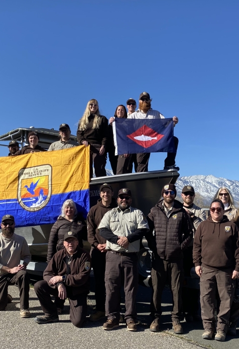 FWS staff on and around boat on trailer on land hold FWS flag, fish pennant 