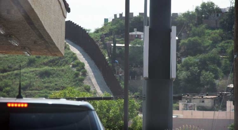 A tall wall is shown on a hillside representing the border between the United States and Mexico.