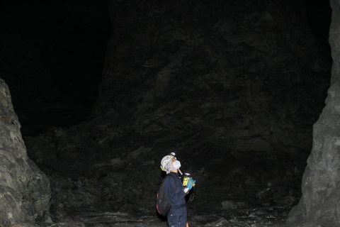 Lone person standing in an underground chamber shining a flashlight and looking up at the ceiling