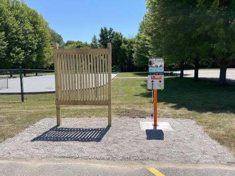 A wooden sign frame next to a cleaning station. A park is in the background.