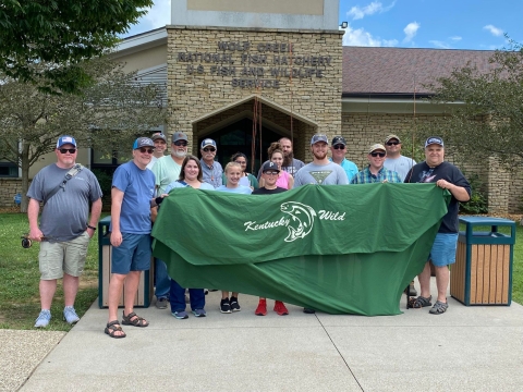 Group photo of people holding a banner in front of facility