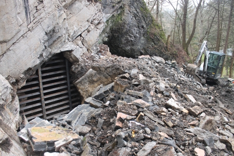 Rock rubble sits to the side of a cave opening covered by a metal grate.