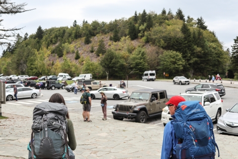 Two people wearing large backpacks on the edge of a parking lot