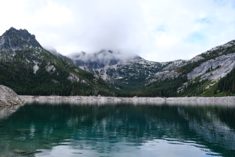 A blue lake with mountains and clouds above it.