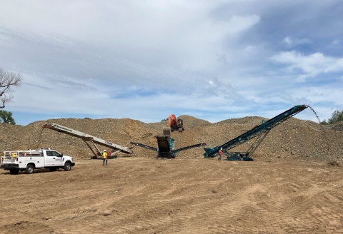 Two individuals operating construction equpment by a dirt mound