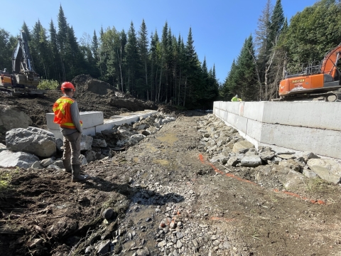 Biologist with hard hat and orange vest overseeing construction of stream bed and bridge abutments on Otter Brook, Maine