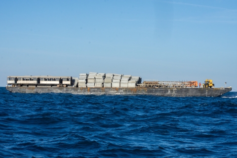 a barge carrying concrete blocks and two old railcars