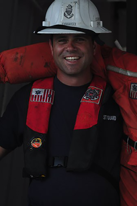 a close up of a coast guard service member wearing a hard hat and a personal floatation device. 