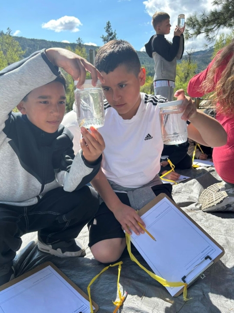two students with clipboards hold small jars with salmon