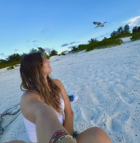 Mady sitting on the beach, taking a selfie with a flying seabird