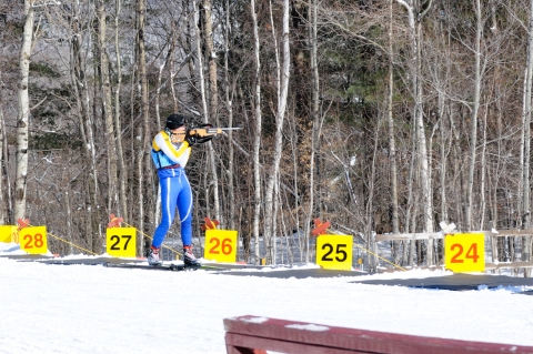 Member of the Massachusetts National Guard Biathlon Team stands in a shooting lane aiming at targets. 