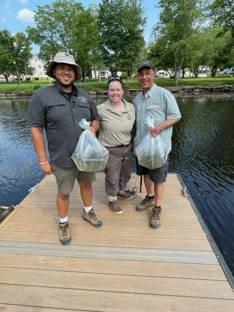 Three people holding fish on a pier above a river.
