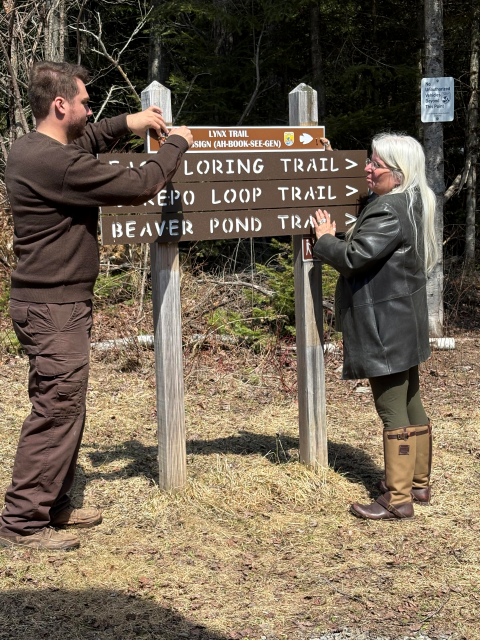 Man and woman attach sign that reads 'Lynx Trail' to wooden posts.