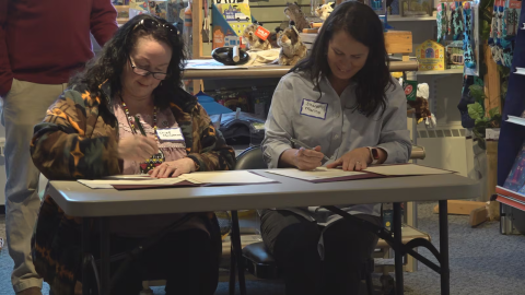 Two women sitting at a table signing documents.
