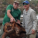 Kevin Enge, left, FWC, and Travis Thomas, UF, right, pose while holding a large male Suwannee alligator snapping turtle with their boat and Suwannee River in the background. This is the 15th year the two men have been trapping and monitoring the Suwannee alligator snapping turtle to conserve and protect them.