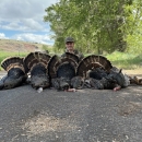 Image of adult man smiling behind vertical line of illegally killed turkeys on ground with sky and hills in background